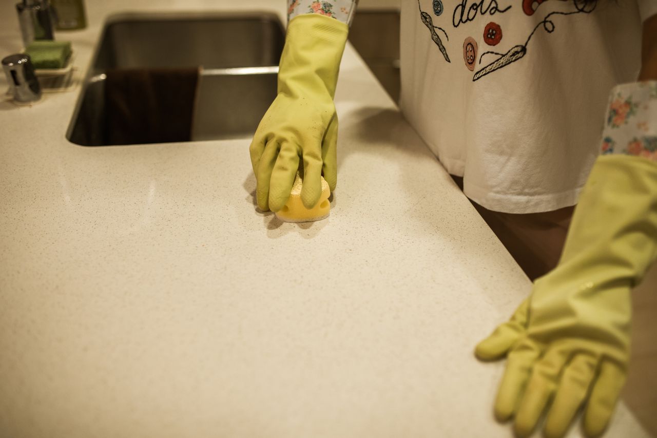 heros-img Woman using yellow rubber gloves to clean a kitchen counter with a sponge.